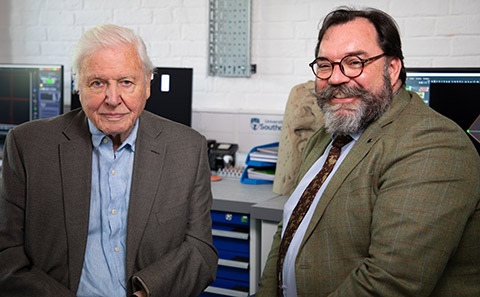 A bearded scientist sits next to Sir David Attenborough.