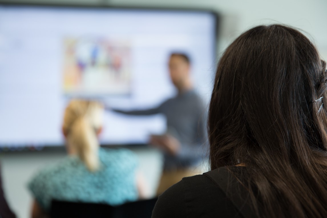 Two people watching a speaker doing a presentation. 