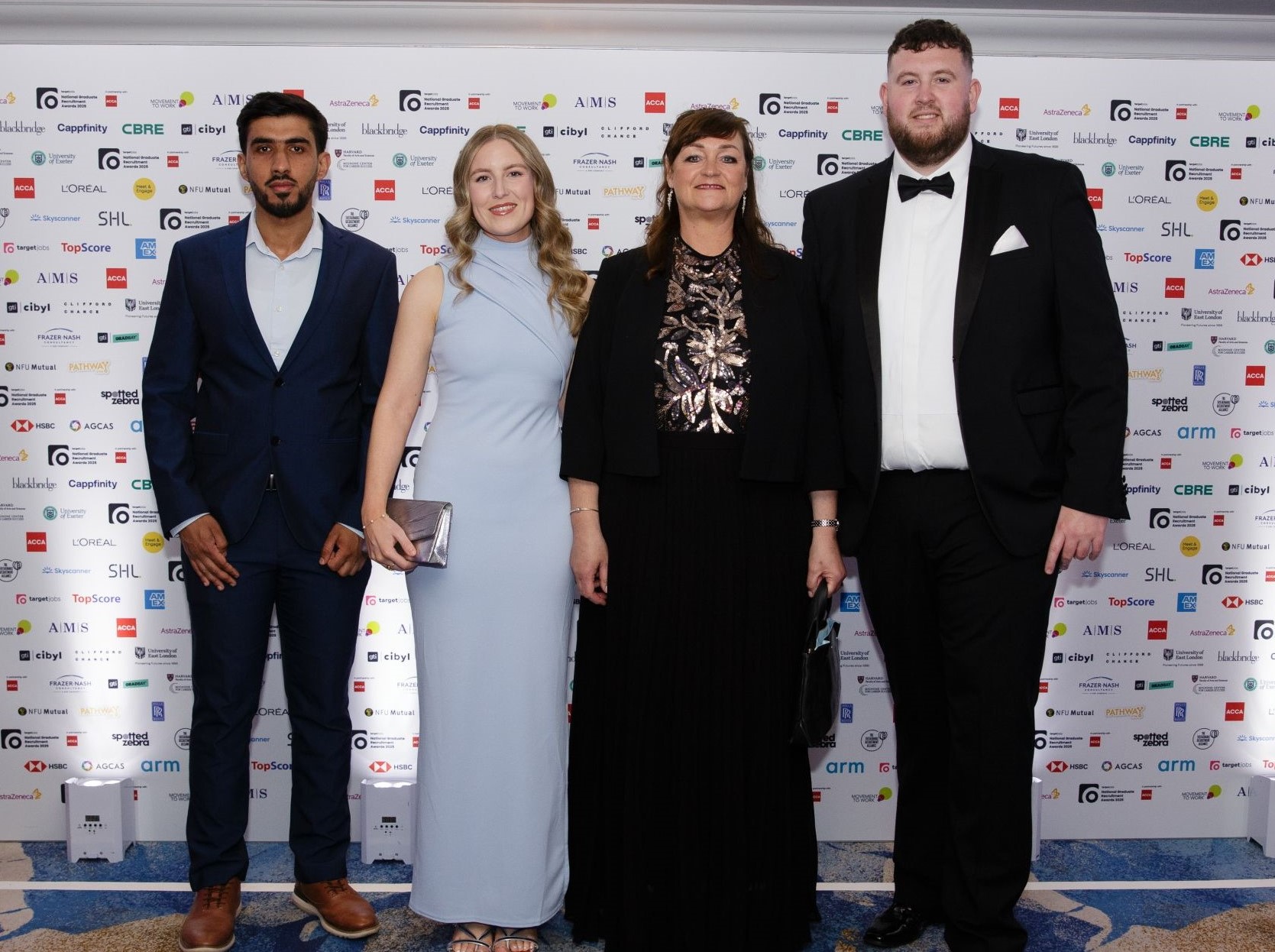 Four winners standing side by side smiling at the camera. They are all dressed in smart evening wear.