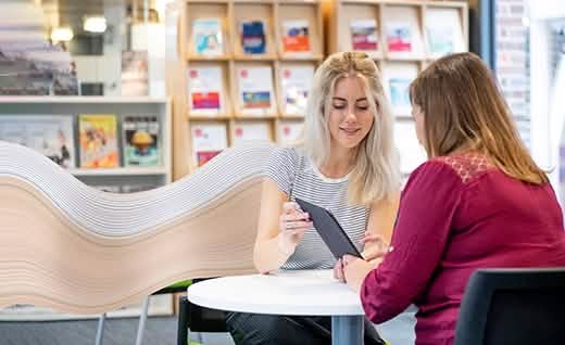 Women discussing in library tablet