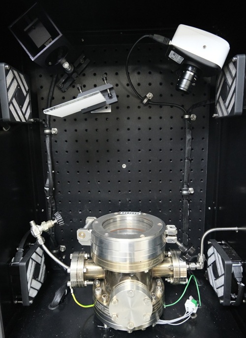 A metallic cylindrical device with a transparent window on a perforated panel, surrounded by cameras and connectors.