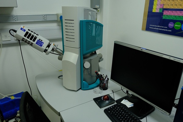 A laboratory desk setup with an electron microscope and a computer monitor.