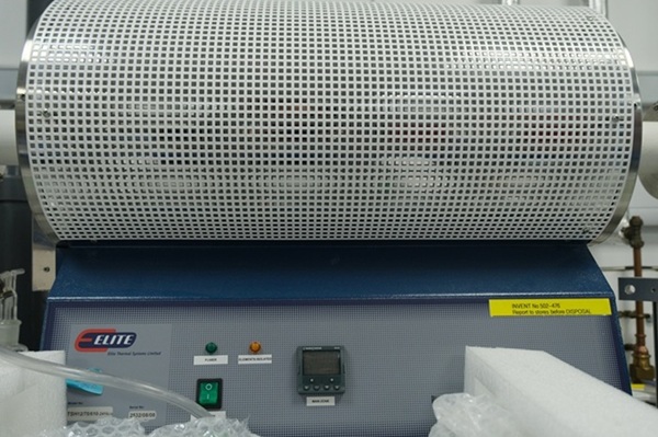 A cylindrical laboratory furnace with a metal mesh cover on a blue control unit with labelled buttons.