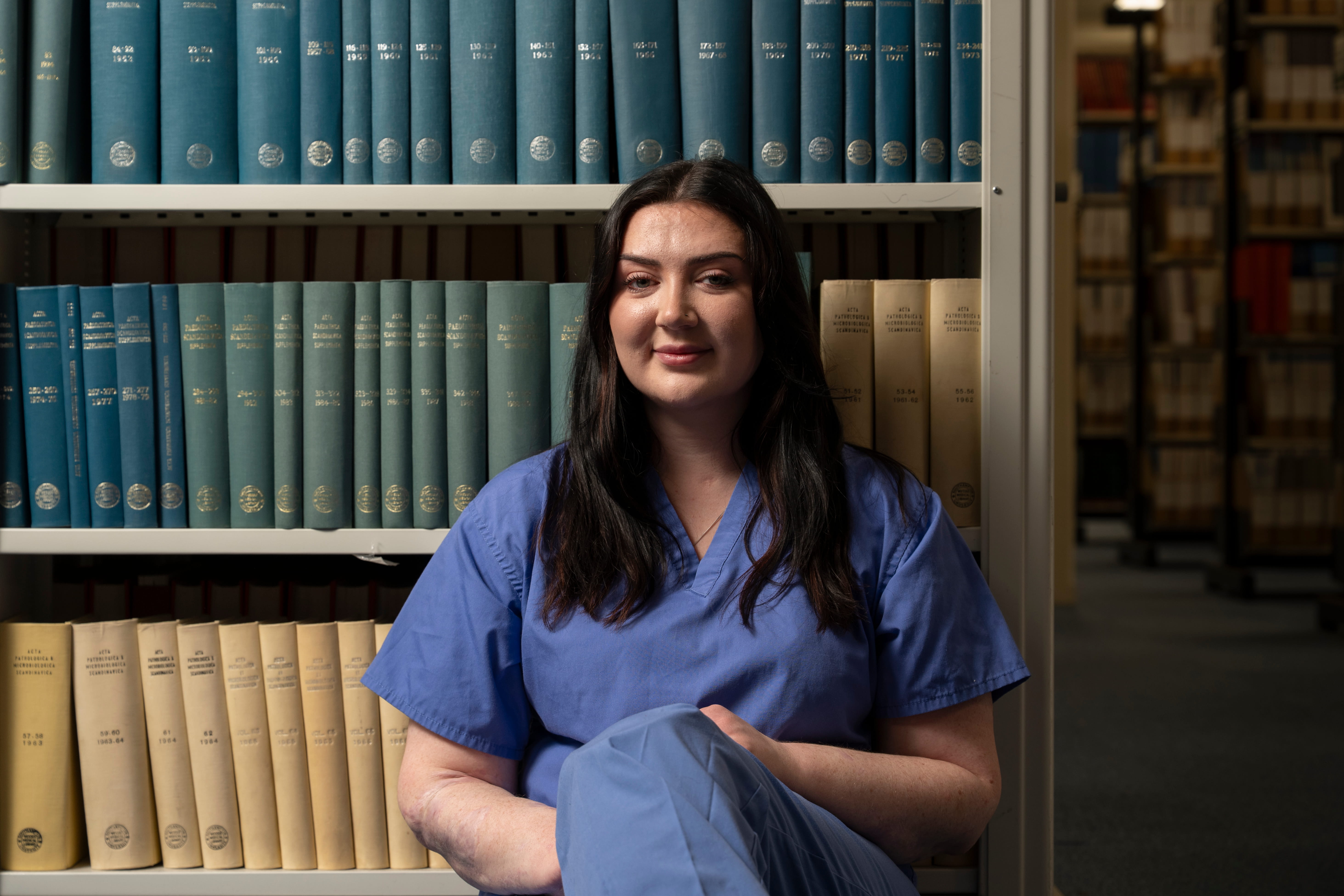 Medical student Becca sitting among library shelves at the University of Southampton Health Services Library.