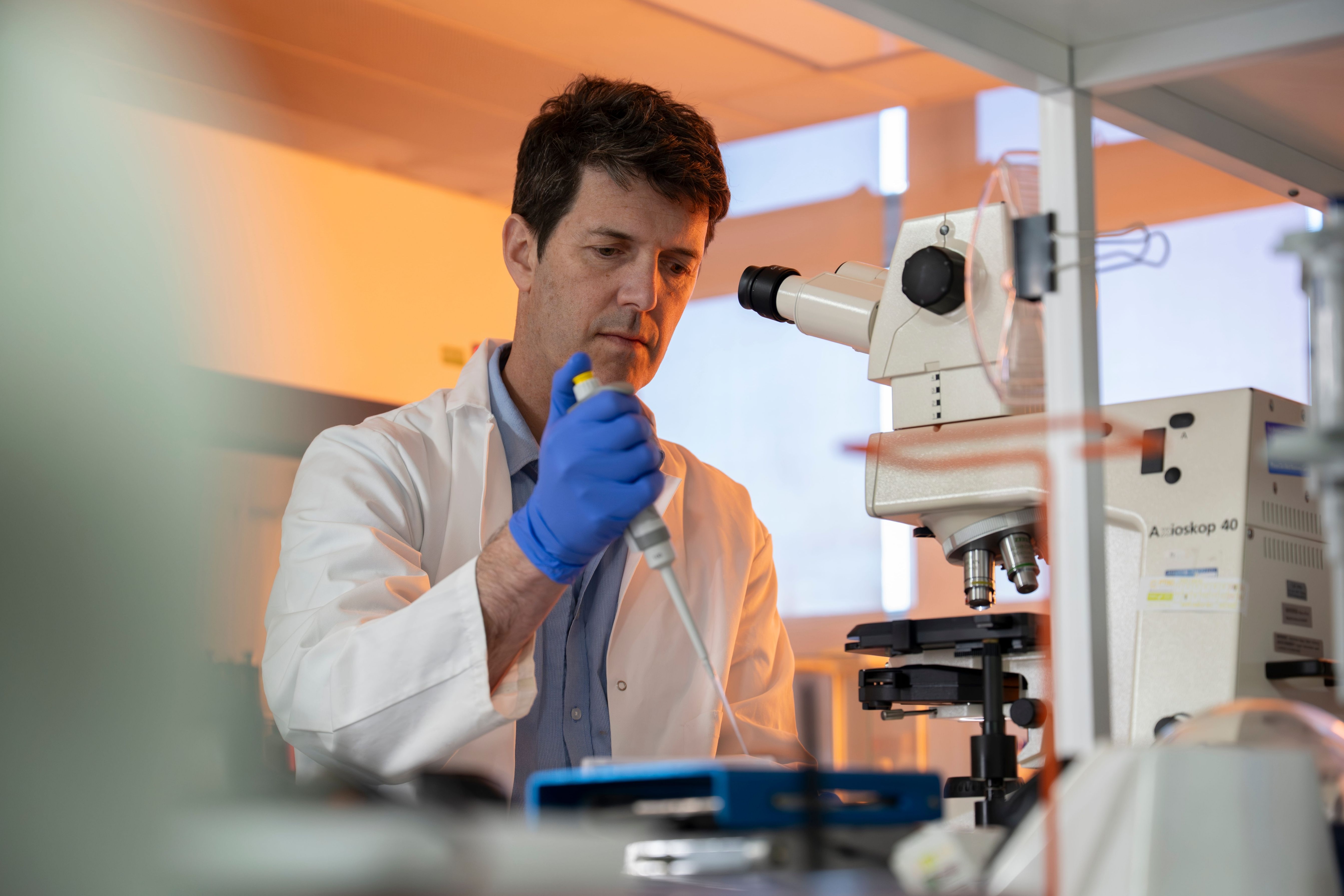 Tom Bibby prepares a laboratory sample beside a microscope.