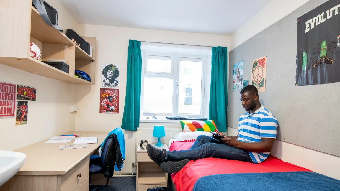 Student sat on bed, working on tablet computer.