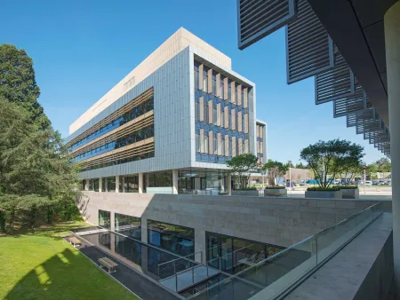 Exterior shot of modern building, surrounded by grass and trees, on a sunny day.