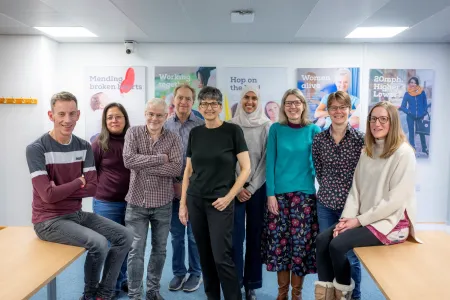 Members of the SHTAC team with Professor Joanne Lord, gathered around a bright room with various posters in the background. 