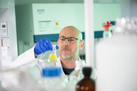 Professor Mark Moore examining a yellow liquid sample in a laboratory flask.