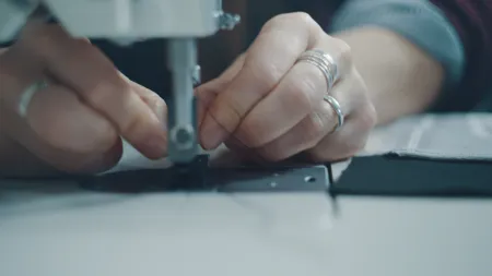 Close-up of hands sewing conductive thread into textile material for wearable technology.