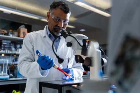 Professor Sumeet Mahajan using a pipette beside a microscope in a molecular biophotonics laboratory.