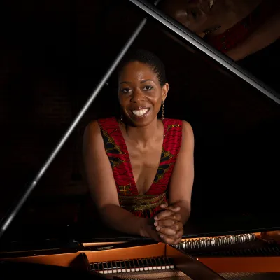 Dr Samantha Ege leaning on a grand piano and smiling.