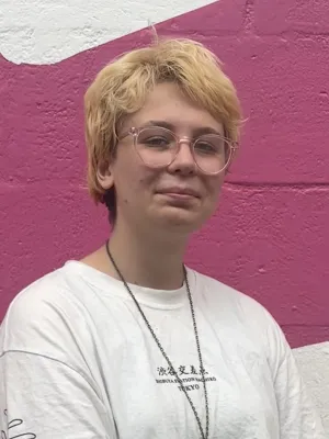 BA Graphic Communication student standing in front of a pink and white painted wall.
