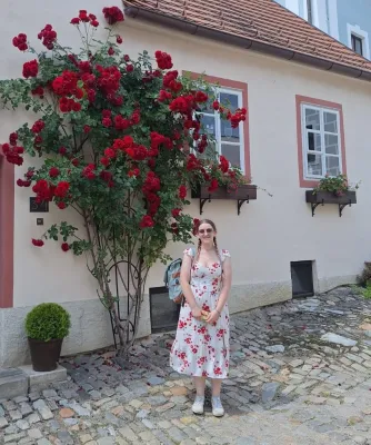 Lucy standing infront of a display of red roses growing up a traditional Czech home.