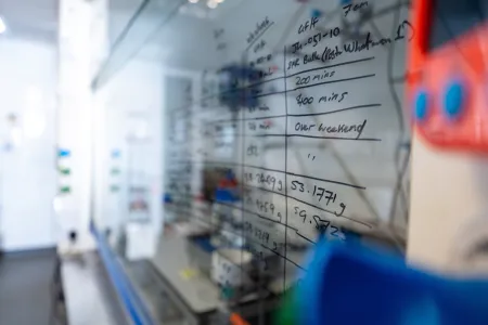 Laboratory research notes and measurements written on a glass board.