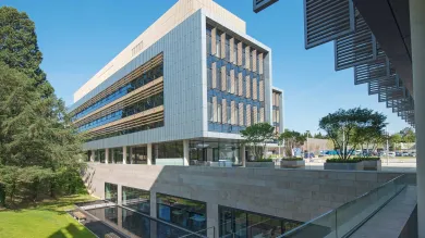 Exterior shot of modern building, surrounded by grass and trees, on a sunny day.