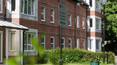 Exterior view of a red brick accommodation building surrounded by grass and hedges on a sunny day.