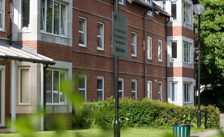 Exterior view of a red brick accommodation building surrounded by grass and hedges on a sunny day.