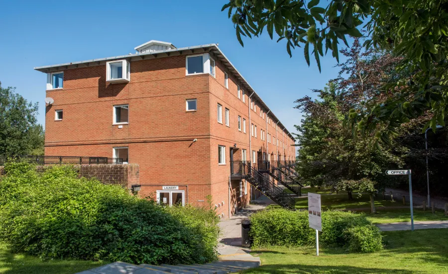 Exterior view of three storey red brick accommodation building surrounded by grass and trees.