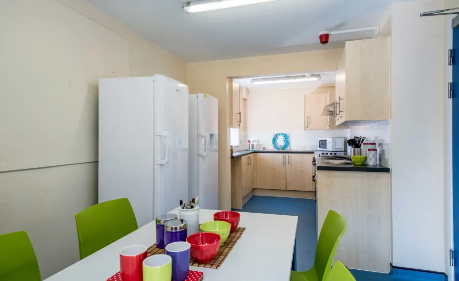 Empty modern communal kitchen with the table set with breakfast cutlery.