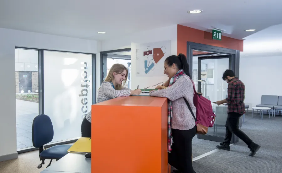 A student talks to a receptionist sat behind a desk in an apartment building lobby.