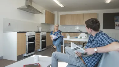 Two students sit and talk in a large, modern, communal kitchen.