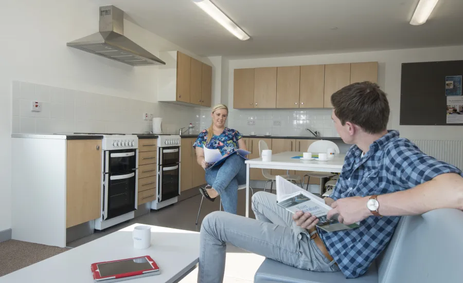 Two students sit and talk in a large, modern, communal kitchen.