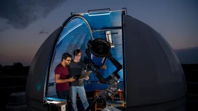 Astronomy students studying data in the shadow of a telescope and rooftop observatory dome.