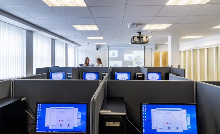 A view of workspaces in the social sciences experimental lab, with two students talking in the background