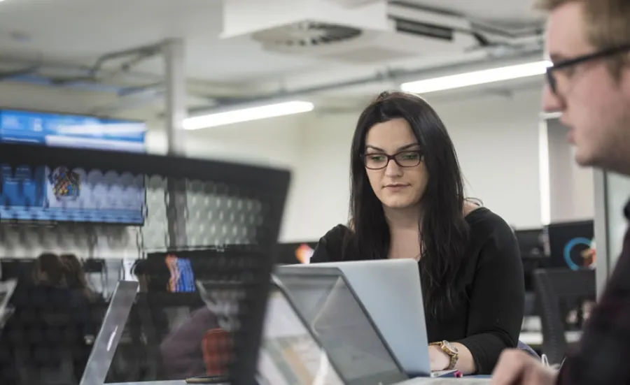 Two students with laptops sharing a table to work on a project together.