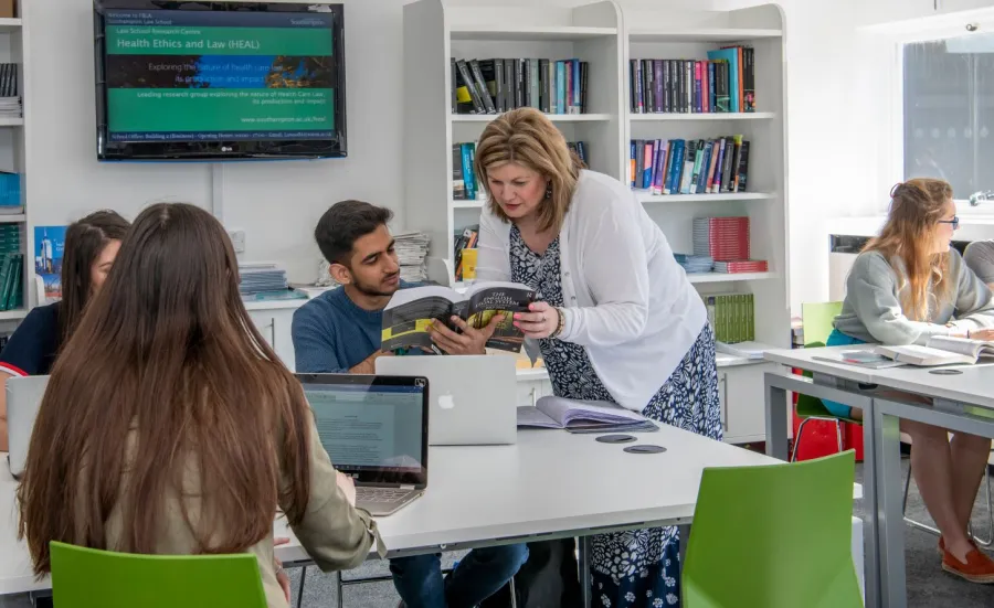 A lecturer teaching law students with laptops and text books in small groups