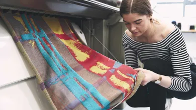 A student crouches by a computerised flat knitting machine as her creation works its way through the mechanism.