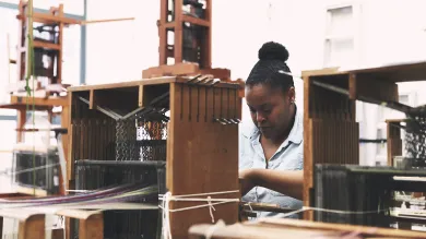 A student weaving at a wooden loom.