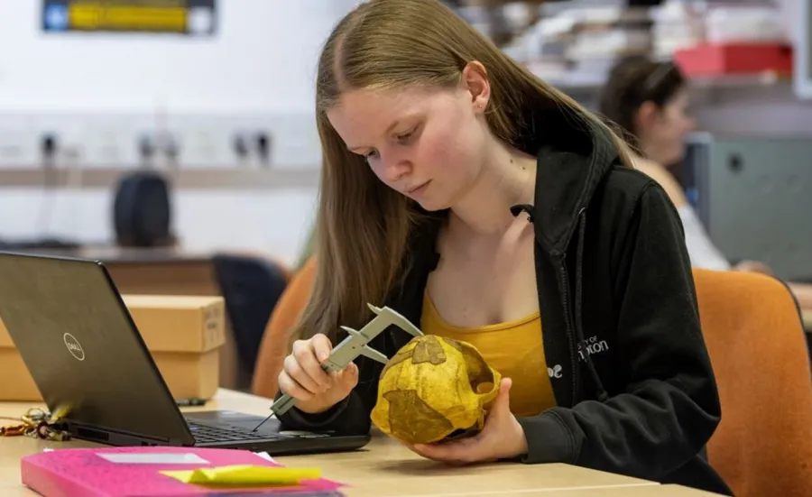 An archaeology student examines an object at a table, using a measuring device