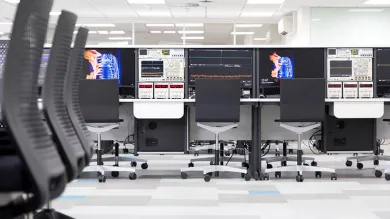A wide shot of various work benches in the laboratory, featuring high-definition monitors and specialised testing equipment.