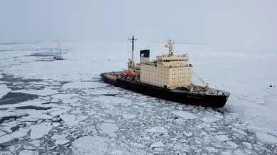 A ship surrouded by ice next to a small vassel.