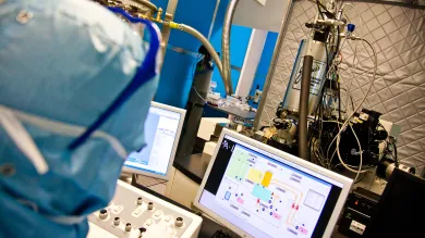 A researcher analysing a complex electrical circuit on a monitor in a cleanroom.
