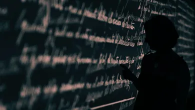 Stock image of a researcher's silhouette set against a wall projection of written language.
