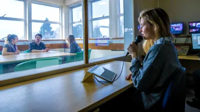 A researcher directs participants of an observation study behind a 2 way mirror