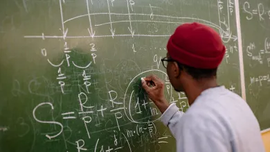 A person with their back to us works out a maths equation on a chalkboard