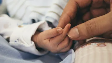 An adult hand gently clasps the hand of a small child