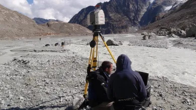 Two researchers sitting together on the ground, surveying data, in a mountain landscape.