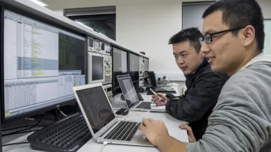 Two cyber security researchers work at a bank of computer screens