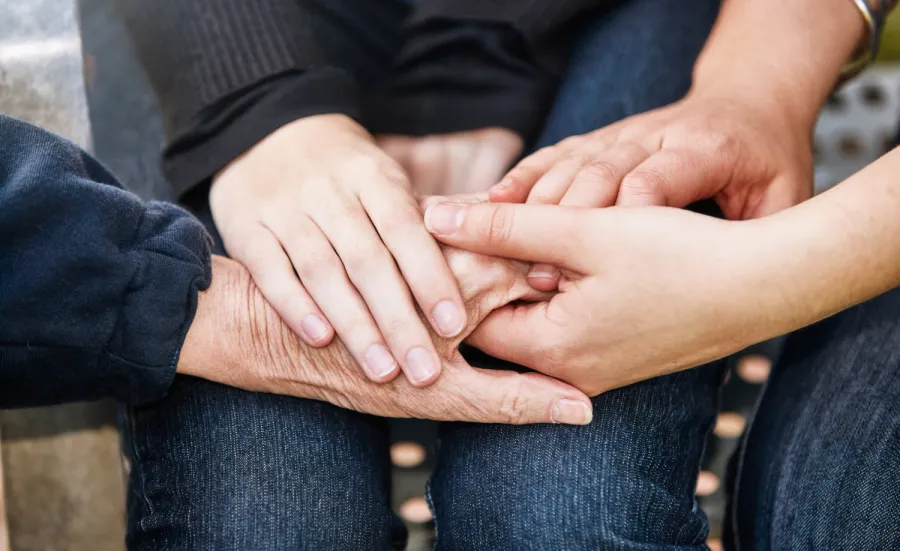 A close up of several overlapping hands holding each other, representing young, mid-life and older generations.