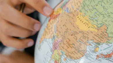The hand of a young person points to a country on a globe model