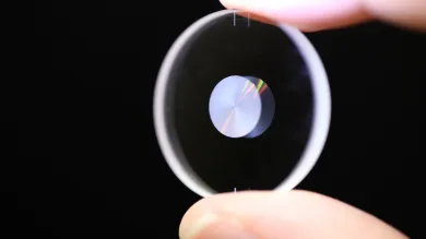 A small optical lens held between a finger and thumb