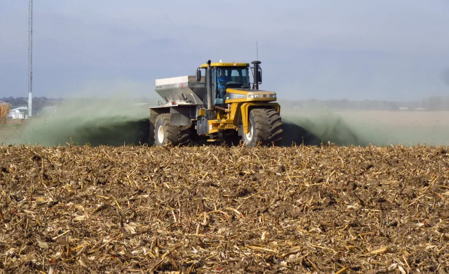 A tractor scattering crushed rock as it drives across a field.