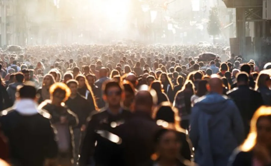 A large crowd of people stretches as far as the eye can see. A low, bright sun highlights a number of individuals who make up the crowd