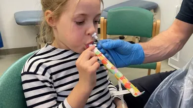 Young girl with a tube up her left nostril, blowing a party blower