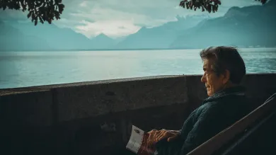 Elderly man sat on a bench next to an alpine lake
